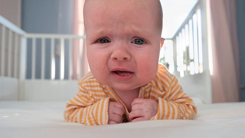 Et billede af en grædende baby i en tremmeseng.