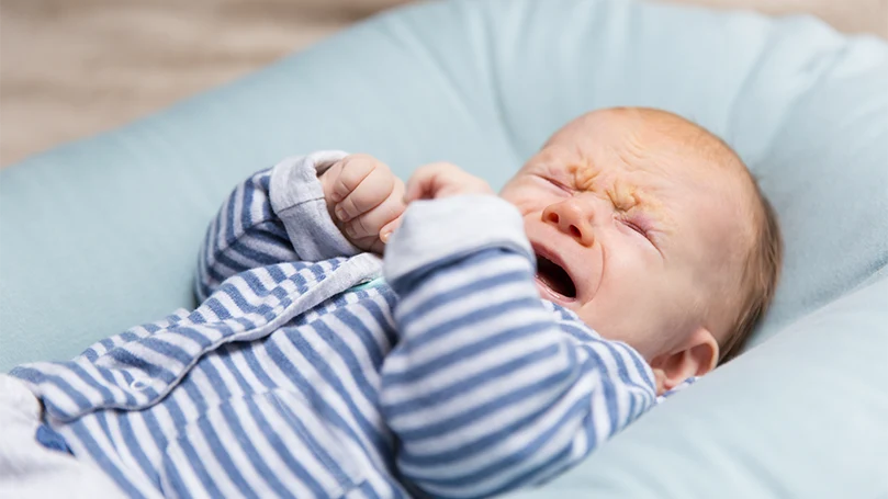 Et billede af en grædende baby i en sengemadras.