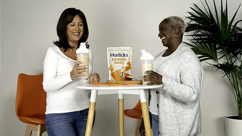 To kvinder står ved siden af et bord og holder glas med horlicks.