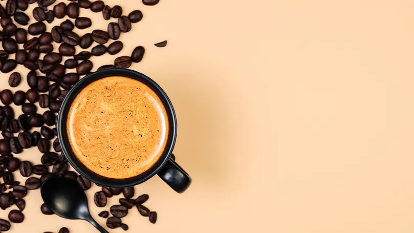 Et billede af en kop kaffe og nogle kaffebønner på et bord.