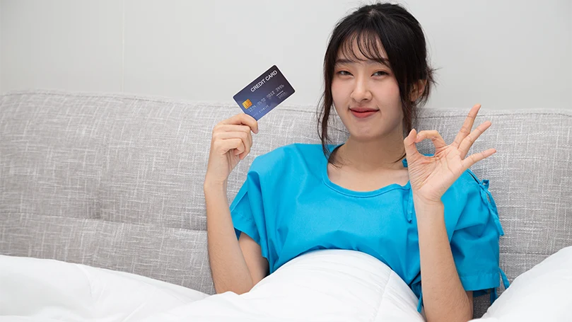 En asiatisk kvinde i sengen holder sit kreditkort