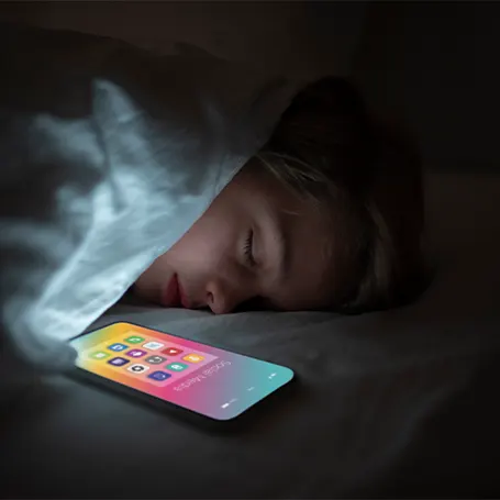 Et billede af et barn, der sover ved siden af en telefon med skærmen tændt.