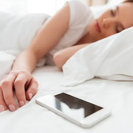 Et billede af en kvinde, der sover ved siden af sin telefon.