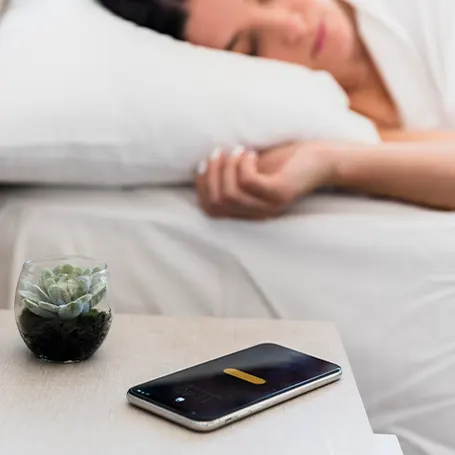 Et billede af en kvinde, der sover med sin telefon på natbordet.