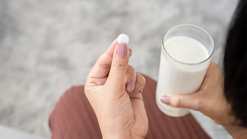 En kvinde tager en melatoninpille med et glas mælk.