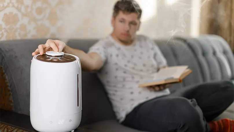 En ung mand læser en bog på sofaen og sætter en humidifer op.